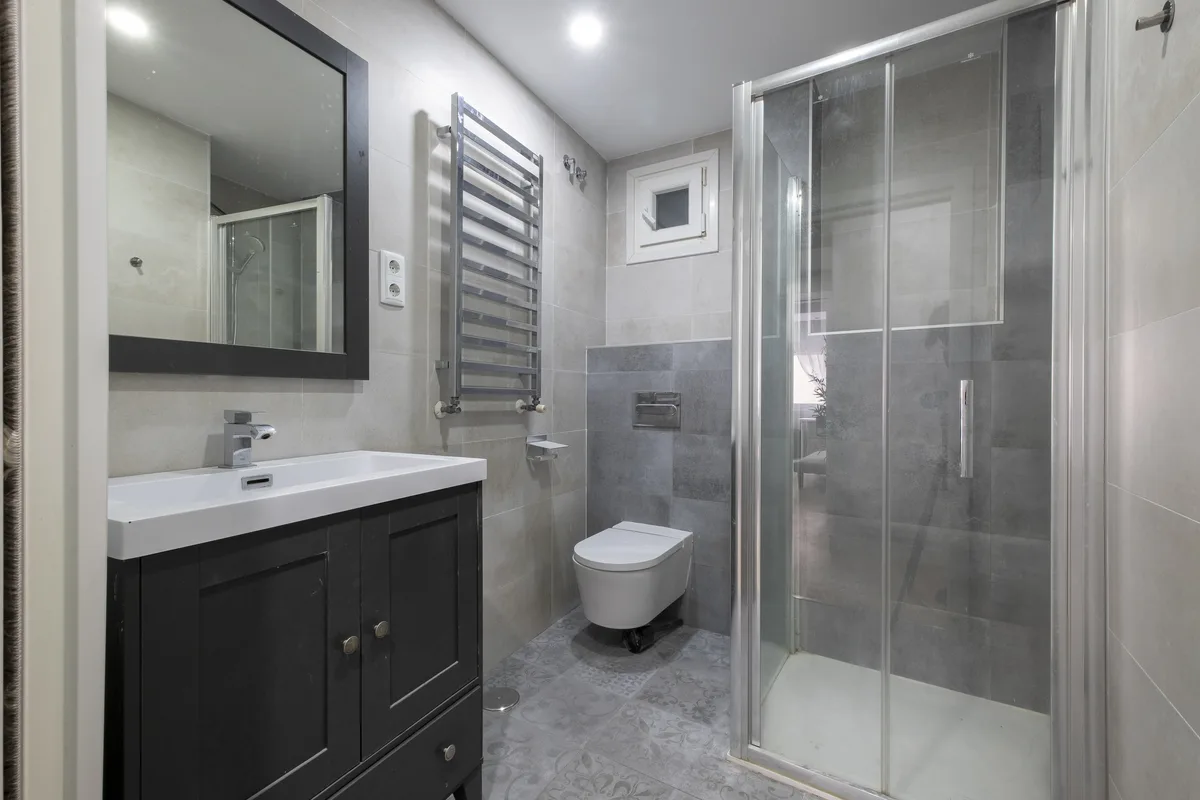 Baño reformado con ducha de mampara de cristal, mueble de lavabo y radiador toallero
